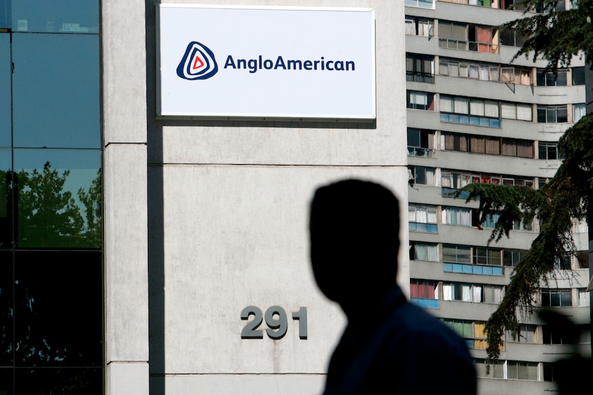 The silhouette of a man walks in front of an office building with the sign for Anglo American.