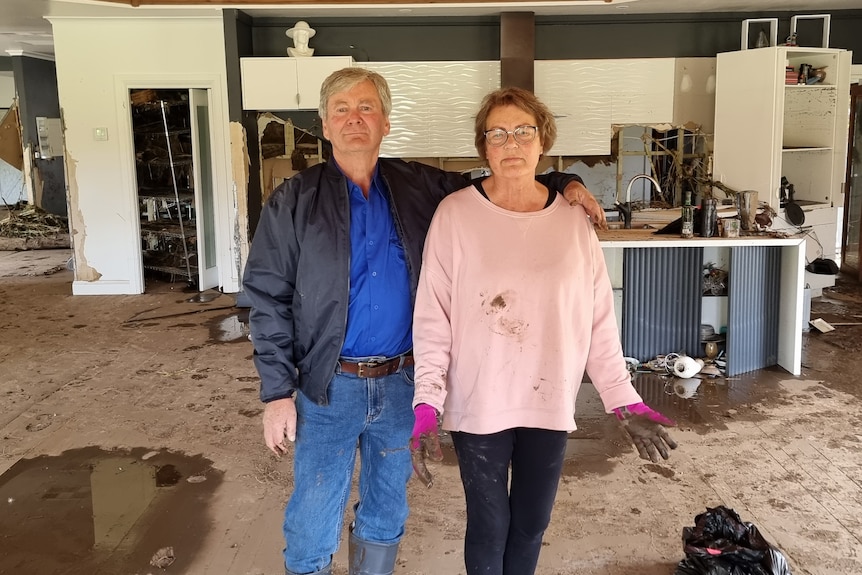 A man and woman stand in their flood-damaged home.