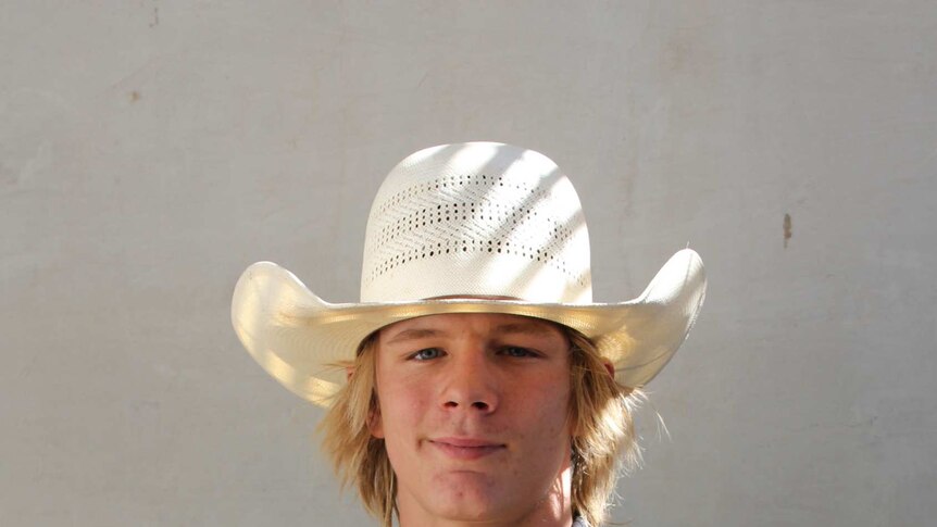 Young man standing in western wear, with a light-coloured wide brim hat.