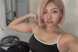 A woman with pink air flexes her arm muscles in a selfie. 