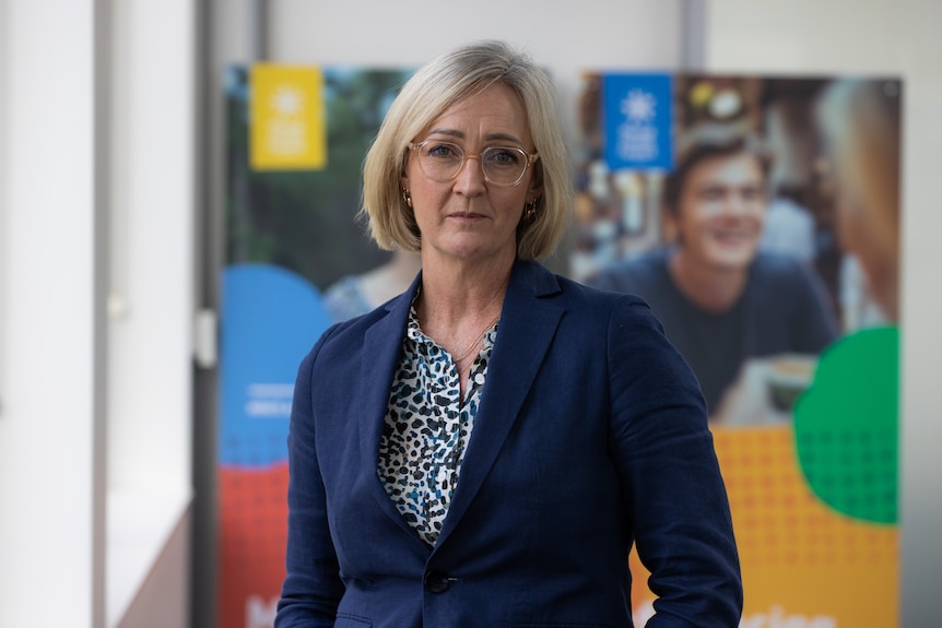 Blonde woman wearing a dark blue suit and glasses 