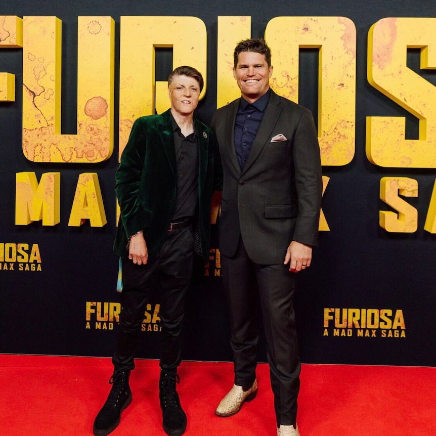 A teenage boy and a man who are both wearing suits stand on the red carpet.