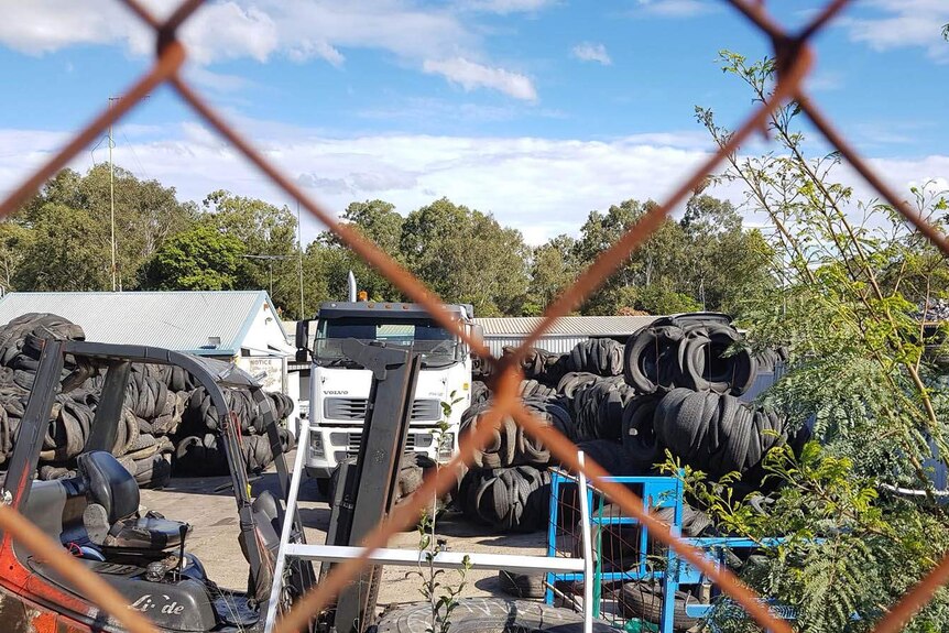 Piles of tyres and a truck behind a rusty cyclone wire fence