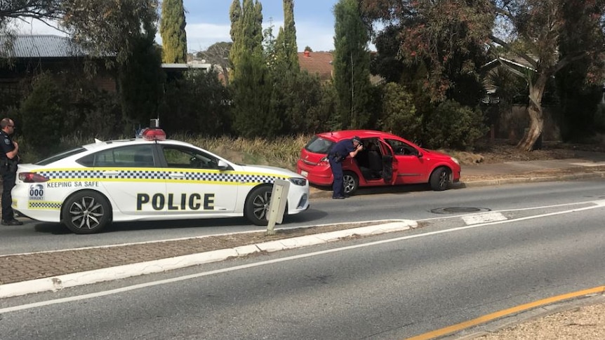 A police car parked on a road behind a red vehicle with a police officer looking inside