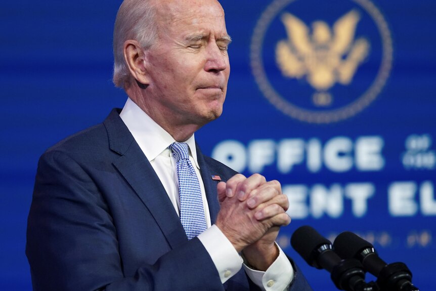 Joe Biden clasps his hands in prayer, eyes closed.