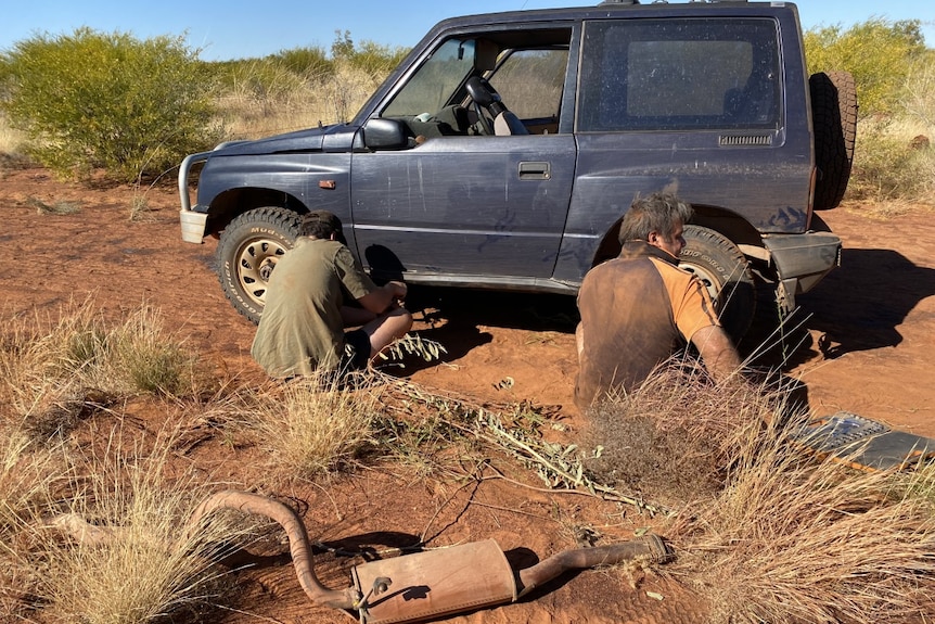 Two people are working on a blue four wheel drive in the desert