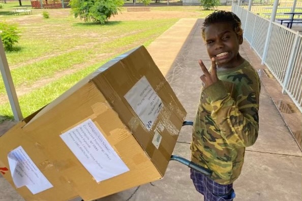 Indigenous boy with box of pre loved sporting gear on trolley