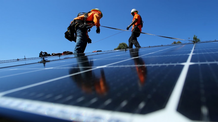 Two men in orange shirts install solar panels on a rooftop.