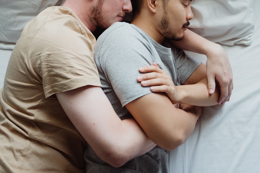 Two men cuddling in bed.