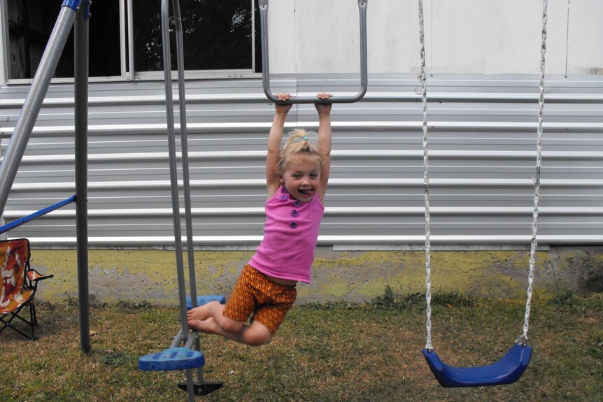 A little girl pokes her tongue out while swinging from a playset outdoors