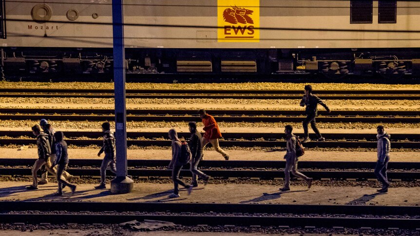 Migrants walk along railway tracks at the Eurotunnel terminal in Calais-Frethun