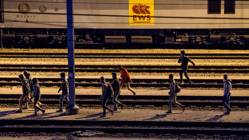 Migrants walk along railway tracks at the Eurotunnel terminal in Calais-Frethun