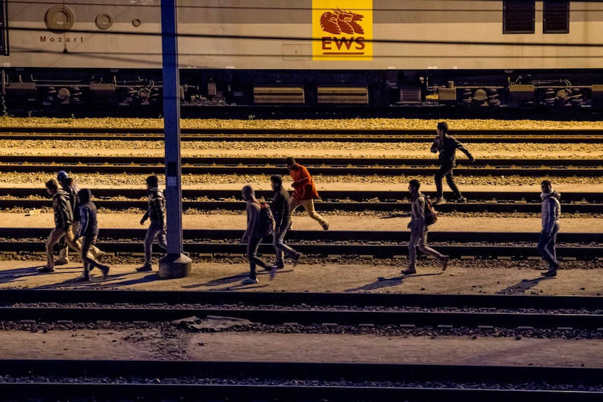 Migrants walk along railway tracks at the Eurotunnel terminal in Calais-Frethun