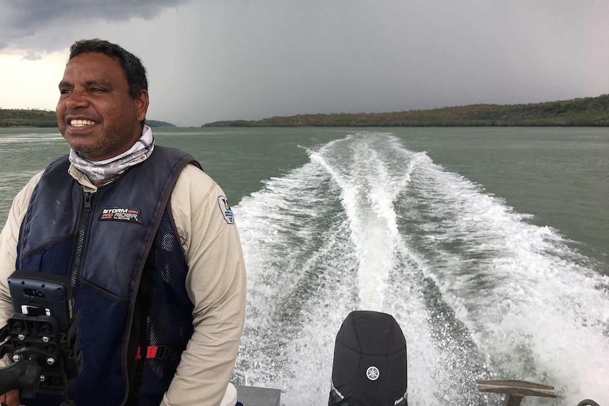 Dambimangari ranger Adrian Lane smiles from the back of a speedboat as it speeds across a river.