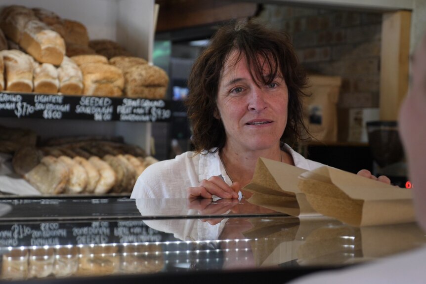 A woman behind a bakery counter giving someone brown bags with food inside