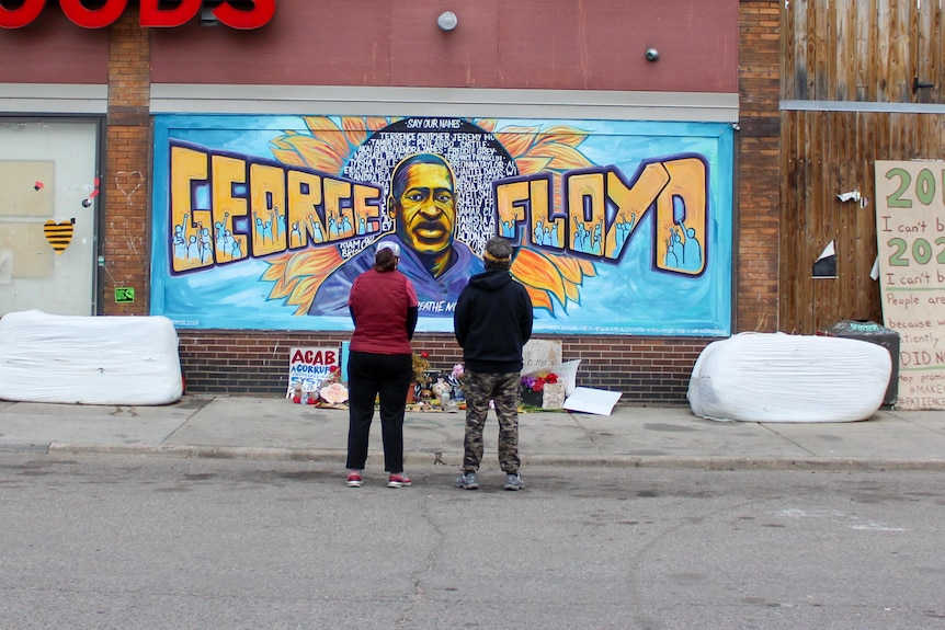 Two men standing in front of a George Floyd mural 