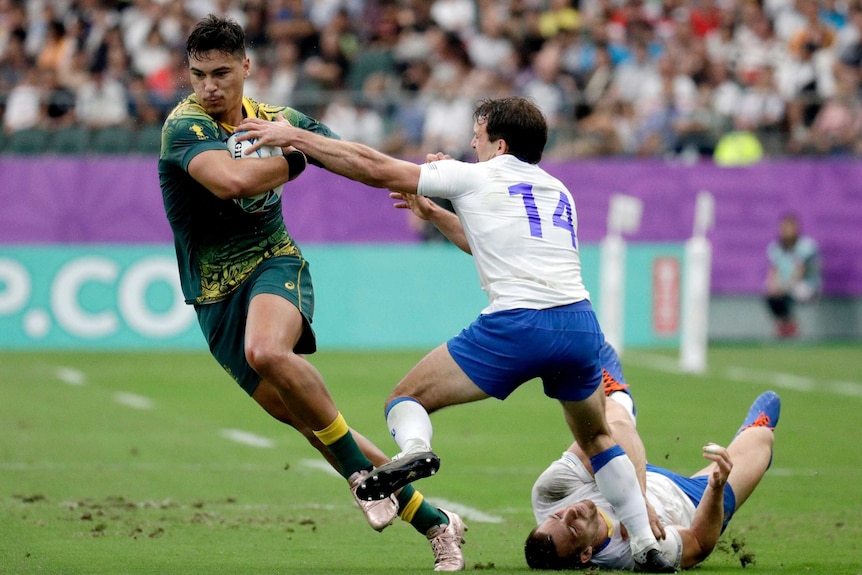 Jordan Petaia runs with the ball under his right arm with his left arm outstretched towards two men in white shirts