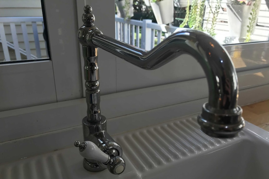 A white sink with an ornate silver mixer tap with a white handle. The tap is in the cold position.