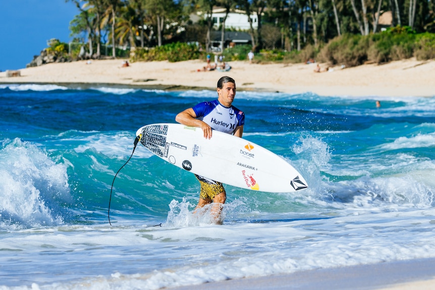 A man exiting the water with a surfboard.