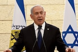 Prime Minister Benjamin Netanyahu speaks next to several Israeli flags