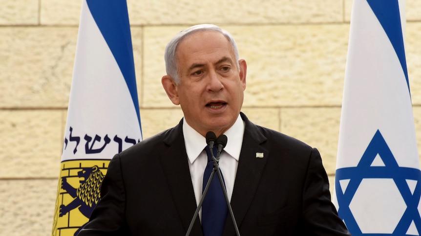 Prime Minister Benjamin Netanyahu speaks next to several Israeli flags