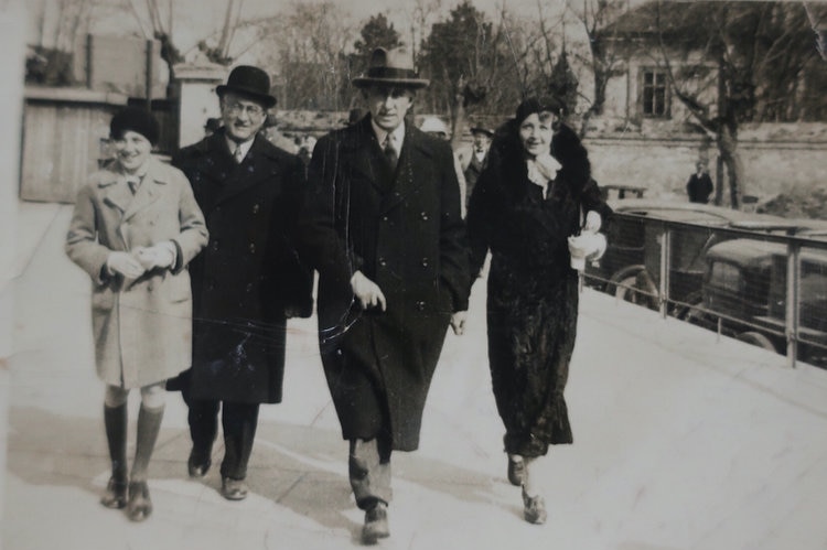 Two men, a woman, and a boy walk towards the camera in an old photograph, they are wearing hats and coats.
