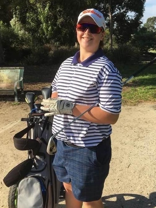 A teenage boy smiling wearing a hat and sunglasses and carrying golfing gear.