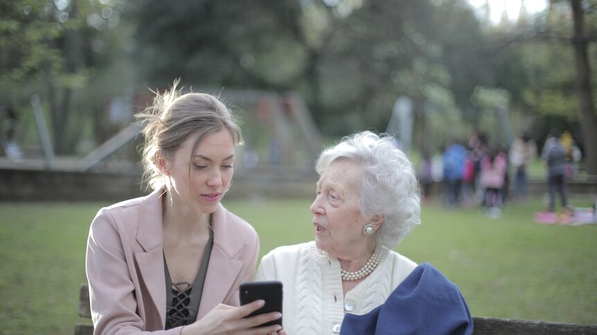 A daughter and her mother in a park looking at a smart phone.