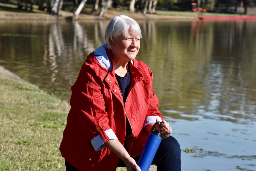 A woman in jeans and a red jacket crouches holding a water testing device.