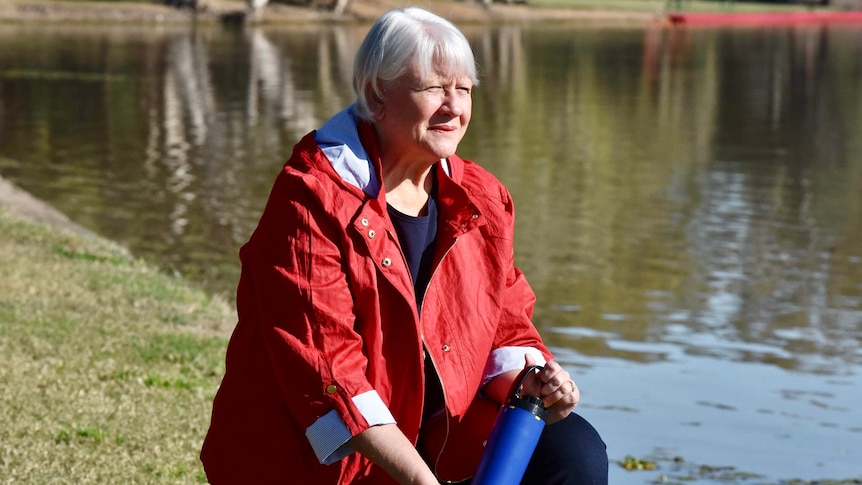 A woman in jeans and a red jacket crouches holding a water testing device.