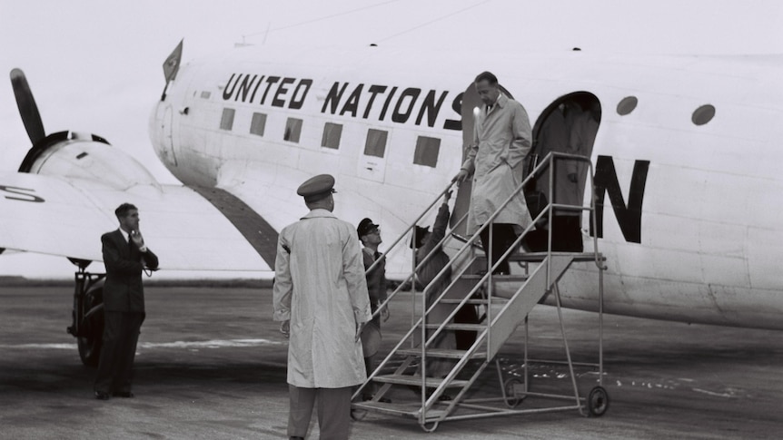 A black and white photo of a man getting off a United Nations plane