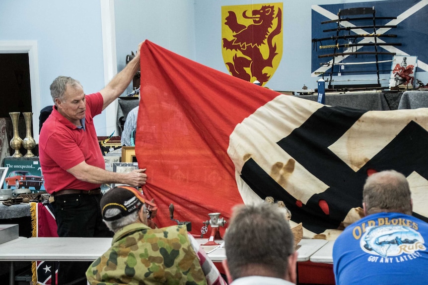 A man holds up a Nazi flag to show a crowd at an auction.