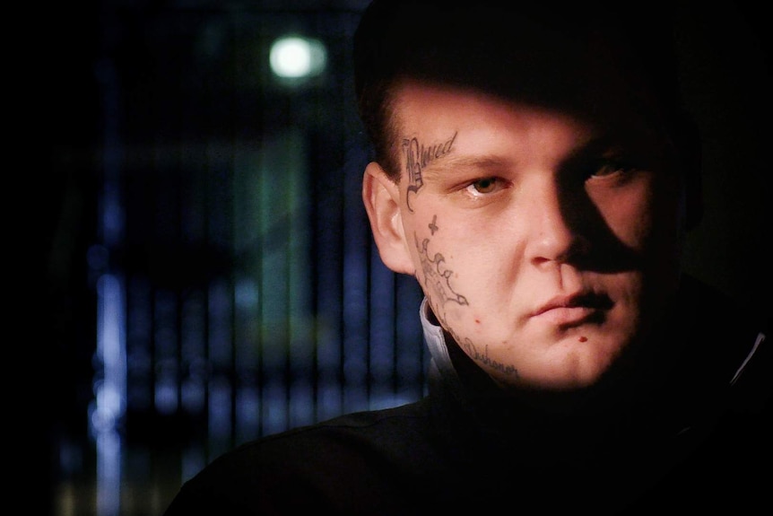 Close up of a young man with face tattoos pictured inside a prison