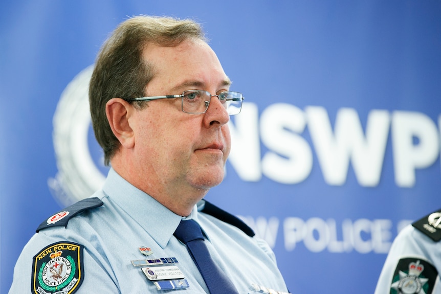 a police officer with glasses standing in front of a big blue sign