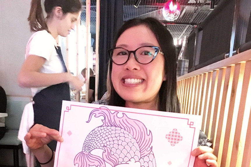 A woman holds up a paper placemat with a fish picture on it in a Chinese restaurant for story on not eating cultural food