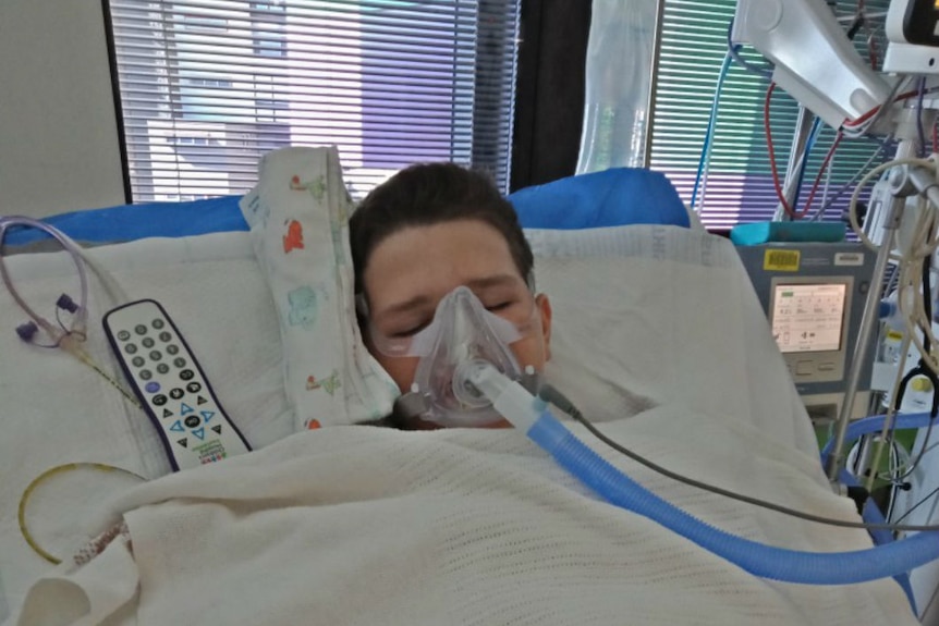 boy in hospital bed with mask over face and tube to medical equipment