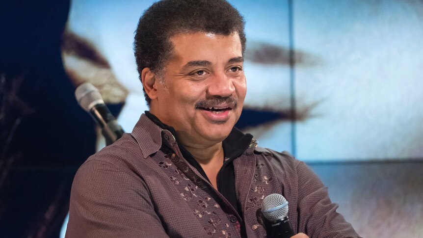 Neil deGrasse Tyson holds a microphone while at a fan event.