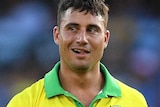 A man wearing a yellow shirt with a green stripe walks towards the camera with a grin on his face