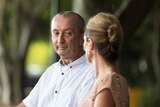 Wayne Griffin sits on a park bench in Brisbane with a female carer beside him.