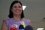 NT Health Minister Natasha Fyles smiles standing behind microphones at a press conference