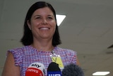 NT Health Minister Natasha Fyles smiles standing behind microphones at a press conference