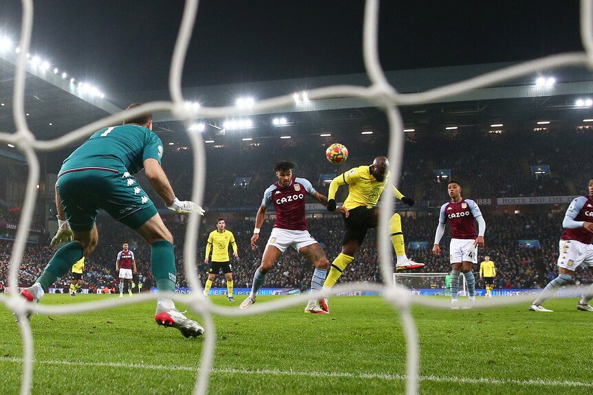 A Premier League striker gets his head to the ball to nod it toward the net past the goalkeeper during a game.
