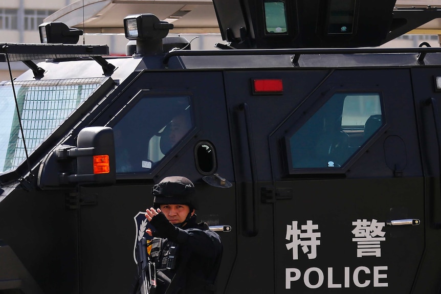 A Chinese police officer stands in front of an armoured police vehicle.