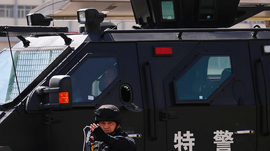 A Chinese police officer stands in front of an armoured police vehicle.