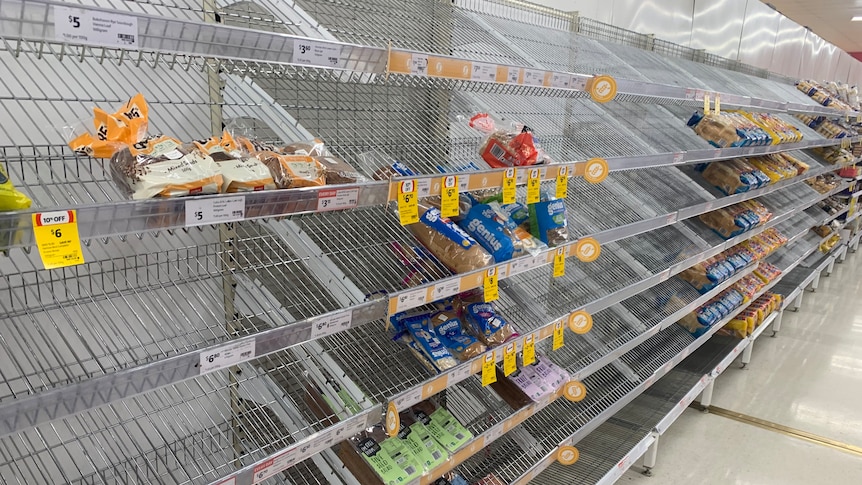 Bread aisle shows shelves mostly empty of loaves.