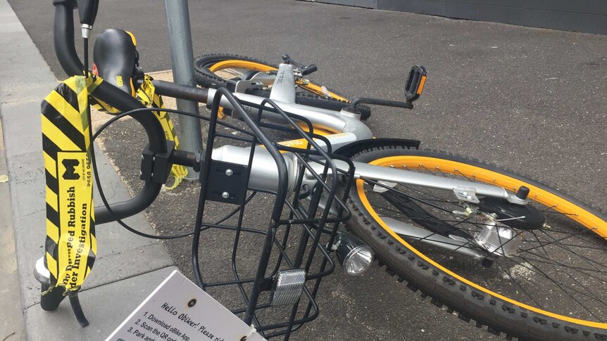 An oBike lying on the street with yellow and black labelling it as dumped rubbish for investigation.