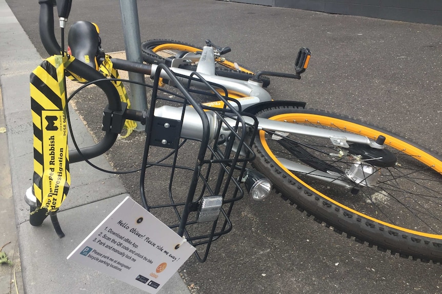An oBike lying on the street with yellow and black labelling it as dumped rubbish for investigation.