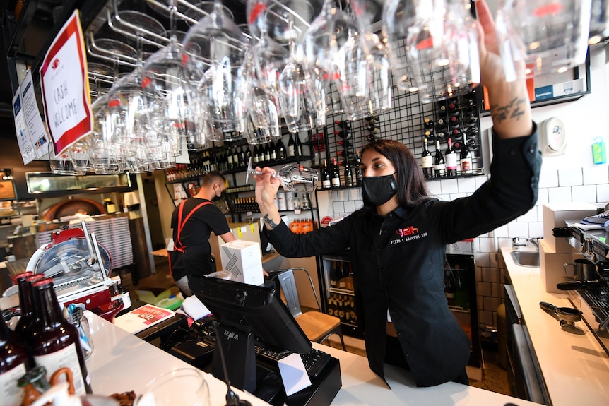 A woman with wine glasses behind a counter.