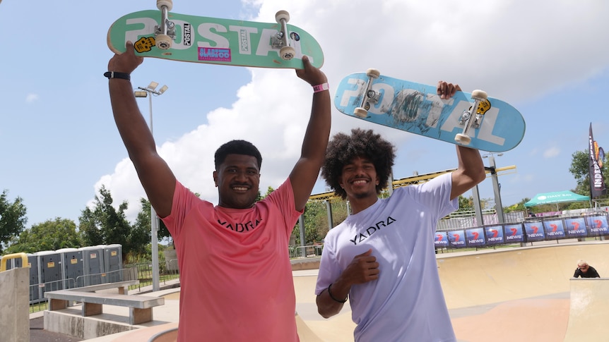 Two Fijian boys hold skateboards above their heads smiling. 