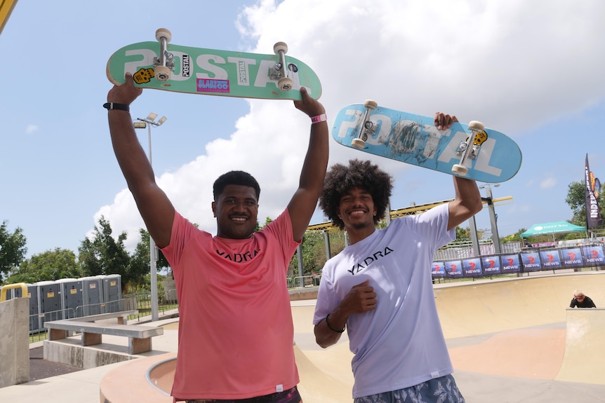 Two fiji boys hold skateboards above their heads smiling. 